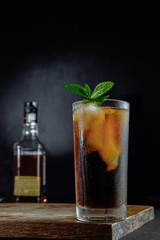 Glass of cola with ice, mint and rosemary on black background