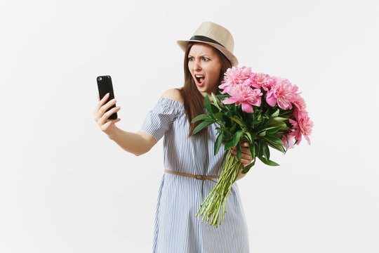 Irritated dissatisfied woman holding bouquet of beautiful pink peonies flowers, doing selfie on mobile phone isolated on white background. St. Valentine's, International Women's Day holiday concept.