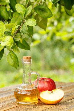 Apple vinegar in glass bottle and fresh red apples on wooden boards with green natural background
