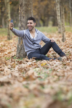 Handsome man in nature taking selfie pictures with his smartphone. Autumn. Copy space