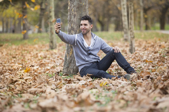 Handsome man in nature taking selfie pictures with his smartphone. Autumn. Copy space