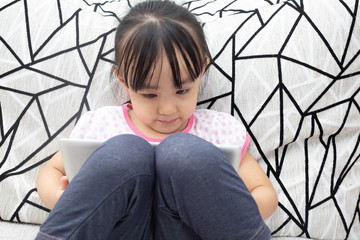 Asian Chinese little girl sitting on the sofa playing digital tablet
