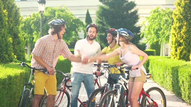 Group of cyclists playing rock-paper-scissors. Four young students stacking hands together in summer park. Friendly team concept.