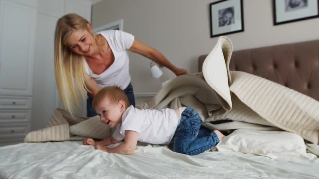 Young mother and father with her 2 years old little son dressed in pajamas are relaxing and playing in the bed at the weekend together, lazy morning, warm and cozy scene. Pastel colors, selective