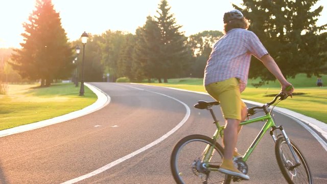 Guy riding bicycle on the road. Young cheerful man cycling on country road, sunny day. Active summer holiday concept.