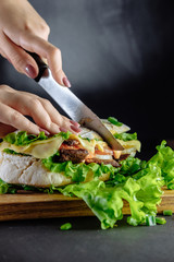 big sandwich on black background Street food, fast food. Homemade burgers with beef, cheese  on the wooden table. Toned image.chef cuts  sandwich knife