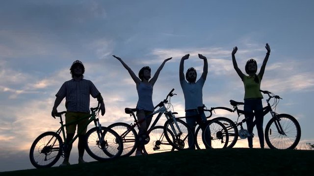 Group of people with bicycles at sunset sky. Four young friends having rest at nature. Amazing trip with bicycles.