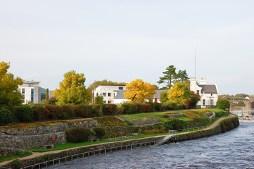 Irish village on the banks of a mountain river; white low-rise houses, a small park on the embankment; autumn