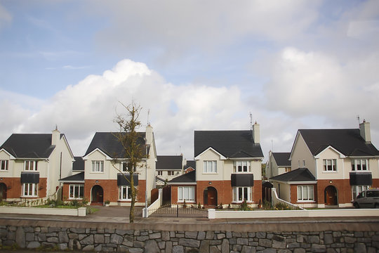 a street view with four identical cottages and a leafless tree, black roofs, red and white two-colored walls, Ireland