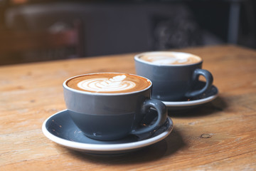 Closeup image of two blue cups of hot latte coffee with latte art on vintage wooden table in cafe