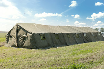 Big military tent in the field agaist bright blue sky