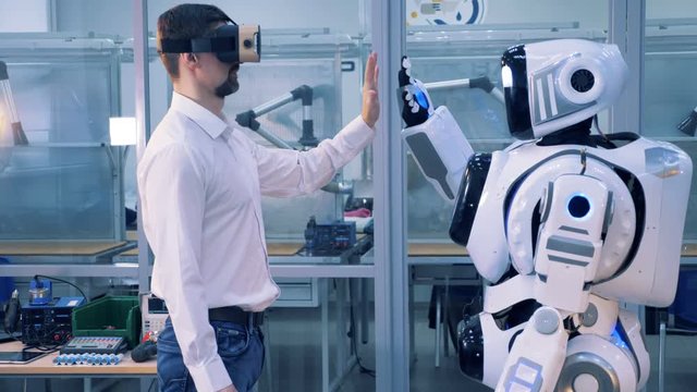 One man in VR glasses gives a robot high-five.