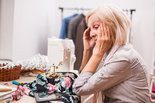 Adult woman is sewing in her studio. She is frustrated because she made a mistake.