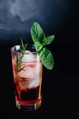 pink cocktail with mint and rosemary on black background close-up