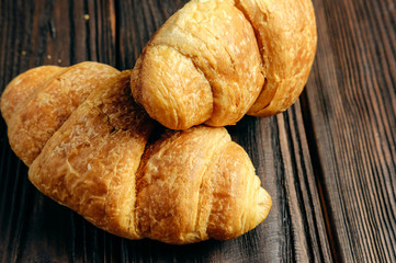two fresh croissants on dark wooden table closeup