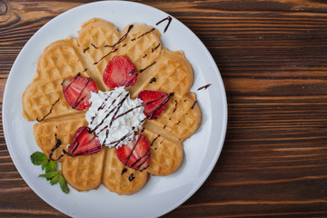  Norwegian heart shaped waffles topped with strawberries,  mint and whipped cream on white plate and wooden background. St. Valentine's Day breakfast. Romantic breakfast. Copy space