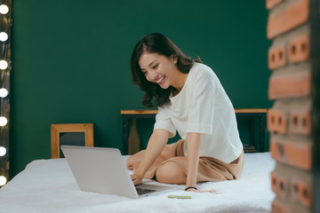 Pretty asian woman using laptop computer in bed in room and smiling