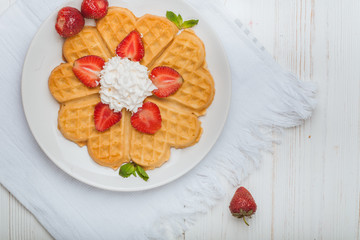  Norwegian heart shaped waffles topped with strawberries,  mint and whipped cream on white plate and white wooden background. St. Valentine's Day breakfast. Romantic breakfast. Copy space