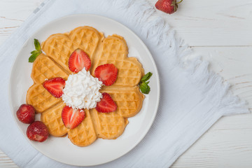  Norwegian heart shaped waffles topped with strawberries,  mint and whipped cream on white plate and white wooden background. St. Valentine's Day breakfast. Romantic breakfast. Copy space