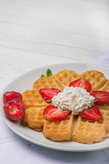  Norwegian heart shaped waffles topped with strawberries,  mint and whipped cream on white plate and white wooden background. St. Valentine's Day breakfast. Romantic breakfast. Copy space