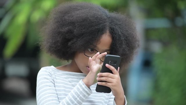 Young cute African girl with Afro hair using phone in the streets outdoors