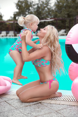 Beauty fashion mother with daughter family look. Beautiful blond woman with having fun with little pretty gil wears in swim wear posing by swimming pool on chill beach. Summer time vacations.