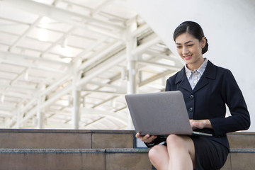 Beautiful cute girl smiling in business woman clothes  using laptop computer  , urban city background