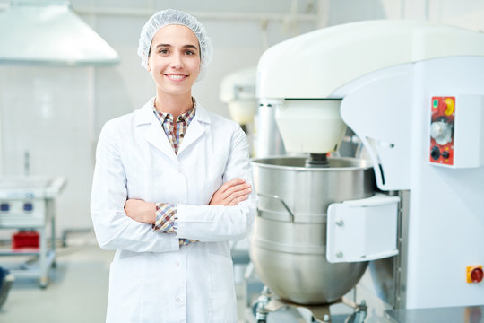 Beautiful Confectionery Factory Worker Standing In White Coat With Arms Crossed Smiling And Looking At Camera.