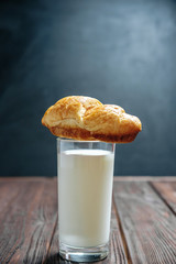 croissant lies on glass of milk on wooden dark table black background
