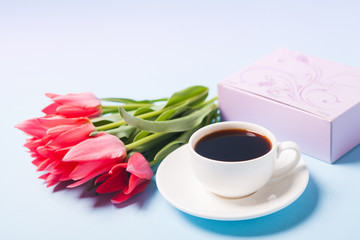 Cup with coffee, bouquet of tulips and pink gift box on a blue background