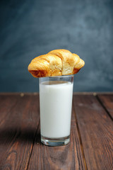 croissant lies on glass of milk on wooden dark table black background