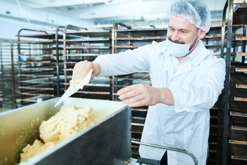 Professional baker in white uniform and mask in process of cooking pastry