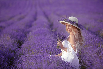 Young blond woman in lavender field. Happy carefree female in a white dress and straw hat enjoying sunset. Outdoors portrait.