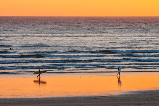 Distant surfers silhouettes on the beach at sunset, Devon, England