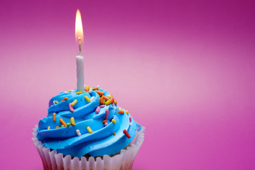 Blue cupcake with candle on color background