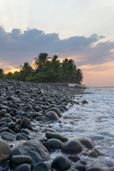 Beach at sunrise with dark rocks in the foreground - vertical.