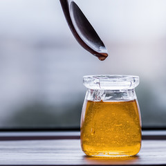 Honey in glass jar and wooden spoon closeup.