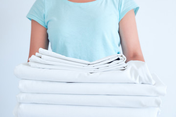 housewife holding a stack of washed bed linen. washing clothes and linen, bleaching of white things.