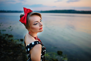 A beautiful young woman dressed standing by the lake, on the background of the sunset