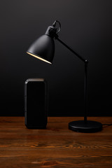 close up view of black audio speaker and lamp on wooden surface on black wall backdrop