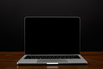 Fototapeta premium close up view of laptop with blank screen on wooden tabletop on black wall backdrop