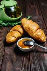 fresh croissants with jam on dark wooden table and tea with rosemary, view from above