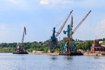 Heavy cranes in cargo port on the riverbank