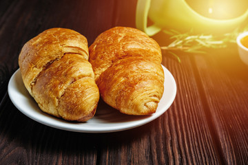 fresh croissants with jam on dark wooden table and tea with rosemary, sunshine