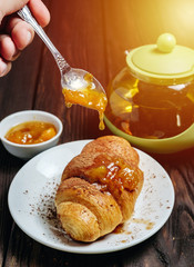 chef pours jam to croissant, fresh croissants with jam on dark wooden table and tea with rosemary, sunshine, chocolate on food