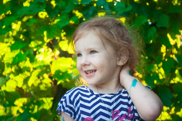 portrait of a cute child, the girls are face on a background of green grape leaves in the summer in the evening light