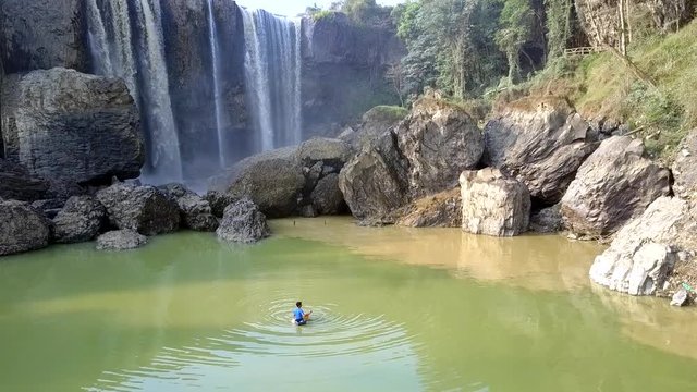 boy fishes in pond sitting on lifebuoy by waterfall