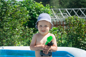 The boy smiles, squints from the sun, the child is satisfied with swimming and swimming in the water in the inflatable pool. The child froze in anticipation. Summer vacation for families