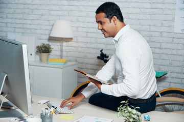Indian businessman sitting on office desk and using pc and tablet computer