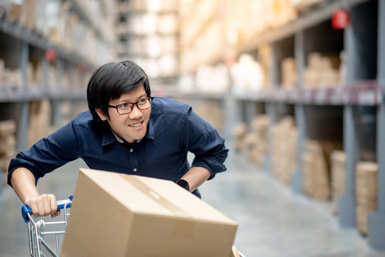 Young Asian happy man using trolley cart putting cardboard box inside. Shopping furniture in warehouse wholesale concept